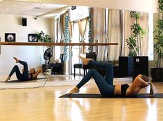 two women are doing exercises on yoga mats in a room with wood floors and large windows