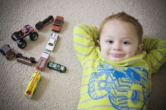 a young boy laying on the floor next to toy cars and trucks, with his hands behind his head