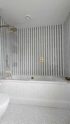 a bathroom with striped wallpaper and white bathtub next to a toilet in the corner