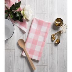 a pink and white checkered table cloth next to utensils, spoons and flowers