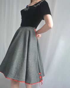 This classic 1950s circle skirt is crafted from a gorgeous quality wool felt. Its heather grey color is accented by peekaboo red trim, including lace-up details at the hem. It was made by Saks Fifth Avenue "The Young Circle" label. It has pockets on either side! It is shown both with and without a crinoline petticoat- you could even wear an even fuller one for that exaggerated 1950s look, but it also looks perfect worn solo. It closes with a zipper and button at side waist. No fiber contents are