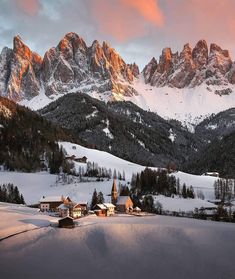 the mountains are covered in snow and there is a small village on the hill next to it