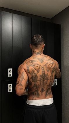 a man standing in front of a locker with tattoos on his back and arms behind him