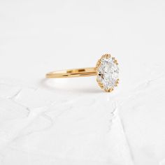 a yellow gold ring with an oval cut diamond in the center on a white background