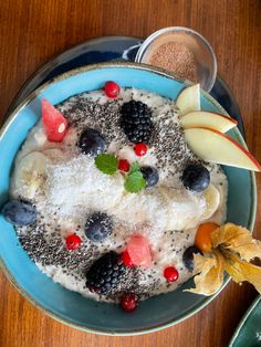 a blue bowl filled with fruit and cereal on top of a wooden table next to an apple