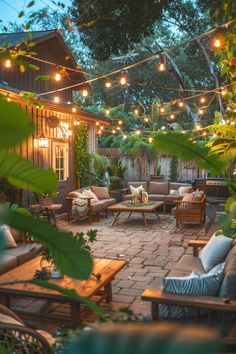 an outdoor patio is lit up with string lights and wooden furniture, surrounded by greenery