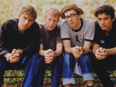 four young men sitting on a bench in the park