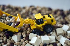 two toy trucks are in the middle of some rocks and gravel, while another truck is on top of it