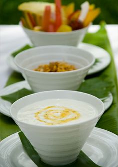 three white bowls filled with soup sitting on top of a green leafy place mat