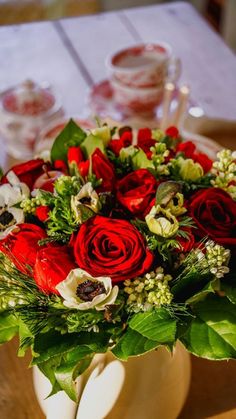 a vase filled with red and white flowers on top of a wooden table next to plates