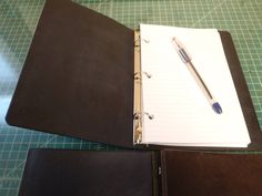 an open notebook with a pen on top of it next to a pair of binders