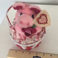 a stuffed pig sitting in a basket next to a measuring ruler on a white table