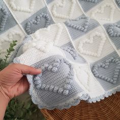 someone is holding up a crocheted blanket on top of a wicker basket