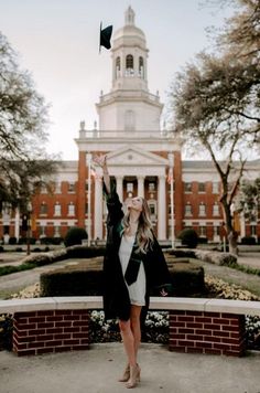 a woman standing in front of a building with her arms up and holding a black graduation cap