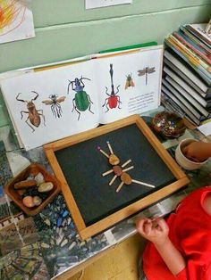 a young boy sitting in front of a book with bugs on it and other children's artwork