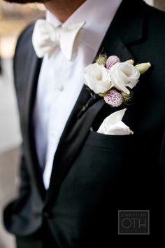 a man in a tuxedo with white flowers on his lapel and bow tie