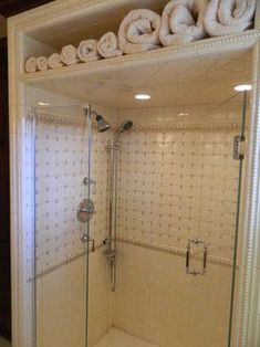 there is a glass shower door with towels on the shelf above it and two rolls of toilet paper