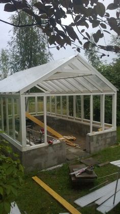 a small white greenhouse sitting on top of a lush green field next to a forest