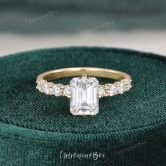 an emerald colored diamond ring sits on top of a green velvet box, with diamonds surrounding it