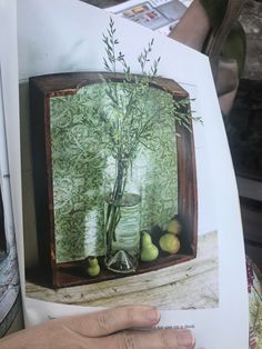 a person holding up a drawing of a vase with plants in it