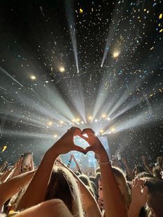 the crowd is holding their hands up in front of a stage with lights and confetti