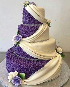 a three tiered purple and white wedding cake with flowers on the top, sitting on a silver platter