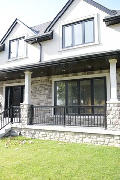 a house that is sitting in the grass with black railings on it's front porch