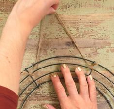 a woman's hand is holding onto a metal ring on a wooden table with wire