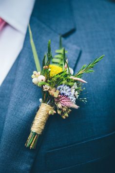 a boutonniere with flowers and greenery on the lapel of a man in a blue suit