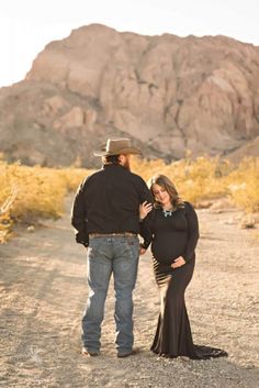 a man and woman are standing in the dirt near a mountain with their arms around each other