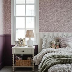 a white bed sitting under a window next to a night stand with a stuffed animal on it