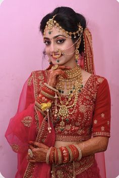 a woman in a red bridal outfit with jewelry on her face and hands to her mouth