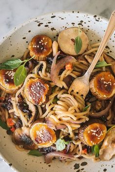 a white bowl filled with pasta and mushrooms on top of a table next to a wooden spoon