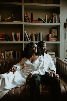 a man and woman sitting on top of a couch next to each other in front of bookshelves