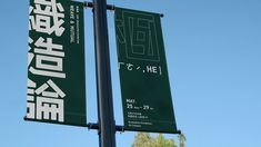 two green and white banners are hanging from a street light pole with trees in the background