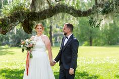 a bride and groom holding hands under a tree