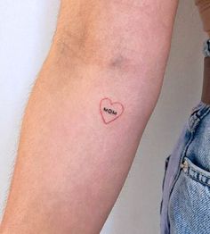 a person with a small heart tattoo on their arm and the word mom written in red ink