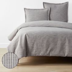 a bed with grey sheets and pillows on top of wooden floor next to white wall