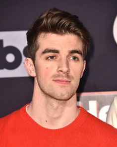 a close up of a person wearing a red sweater and looking at the camera with a serious look on his face