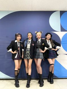 four girls in school uniforms standing next to a blue and white wall with an advertisement behind them