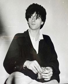 a black and white photo of a woman sitting on a bed holding a glass in her hand