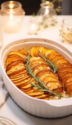 baked potatoes with rosemary sprigs in a white casserole dish on a table