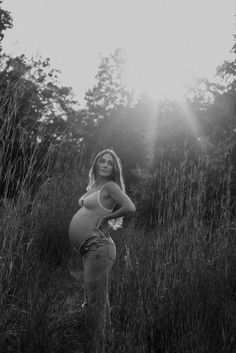 a pregnant woman standing in tall grass with her hands on her hips