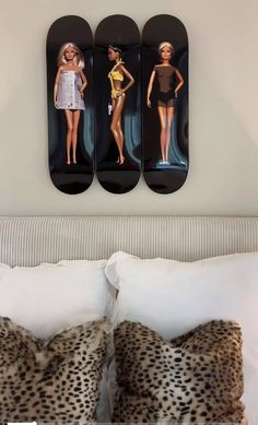 there are three barbie dolls on the wall above the bed, and two pillows in front of them