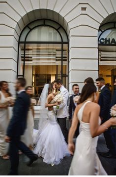 a bride and groom kissing in front of a building with many other people walking by