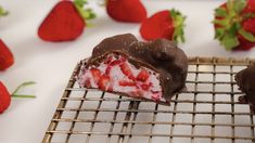 two chocolate covered strawberries sit on a cooling rack next to some fresh strawberries