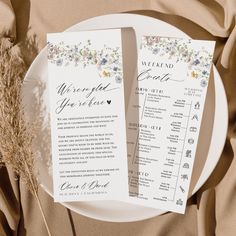 two wedding programs on a plate with dried flowers and greenery next to it, sitting on a tan cloth