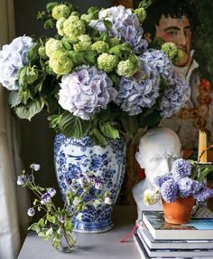 blue and white flowers are in a vase on a table next to two books with a man's face behind them