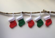 four knitted christmas stockings hanging from a twig on a tree branch, with white and green stocking