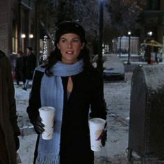 a woman standing in the snow holding two cups